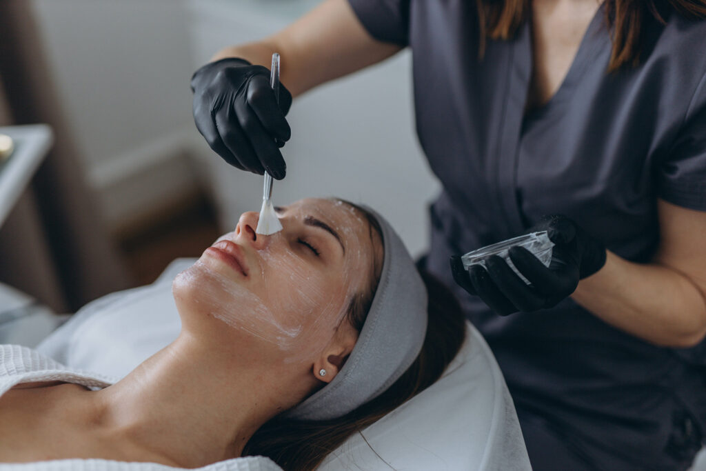 Cosmetologist performs a facial peeling procedure on a young woman.