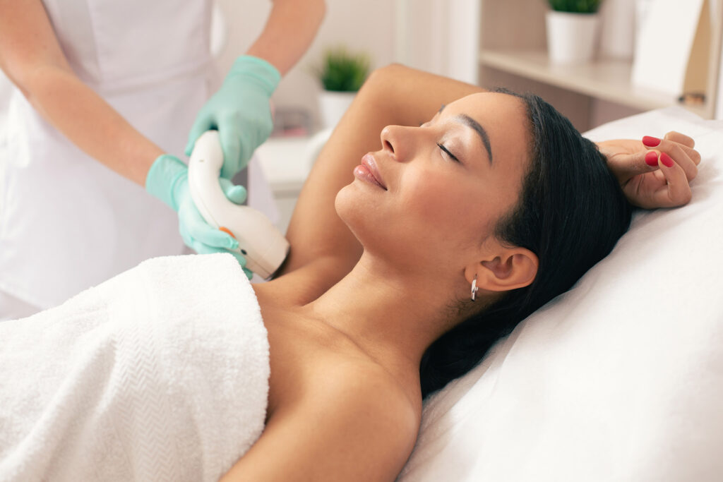 Calm woman lying with her eyes closed and having laser hair removal with a vacuum suction on her armpit