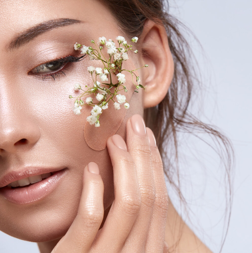 gorgeous woman close-up with green plants under plaster on her cheek, copy space, natural facial treatment, eco beauty concept