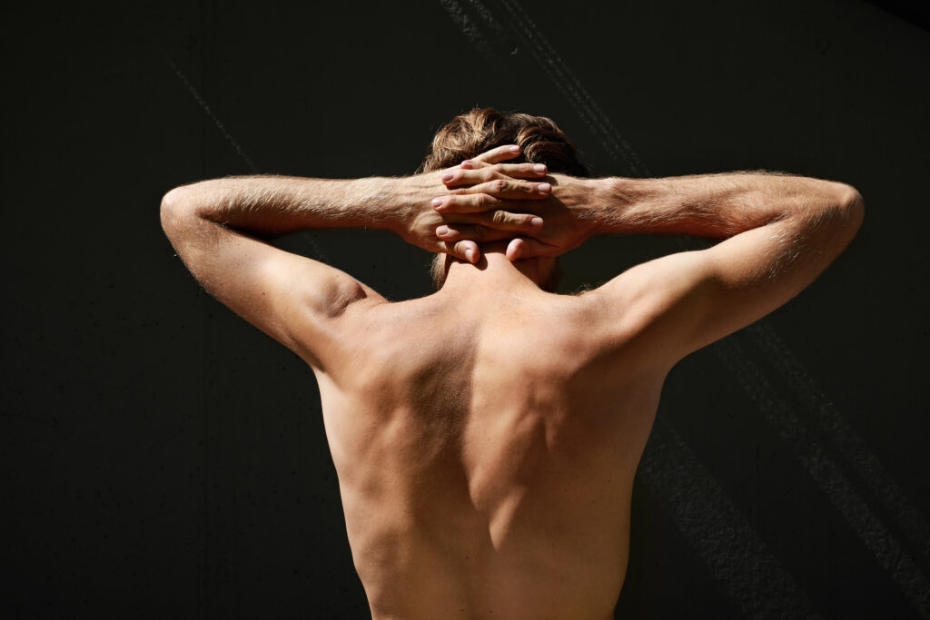 Perfect fit man from the back with crossed arms. Dark background. High quality photo.