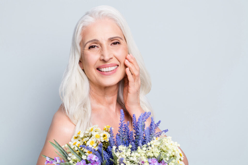 Photo of beautiful retired woman hold big bunch wild flowers touch cheek floral cream isolated grey color background.
