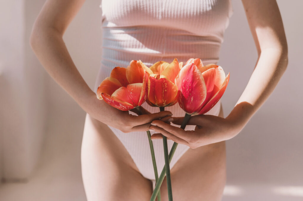 Young woman holds tulip near bikini zone