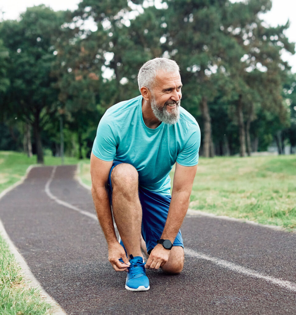 Portrait of a happy active mature or middle aged senior man posing fixing shoelace on his running shoe after exercising outdoors