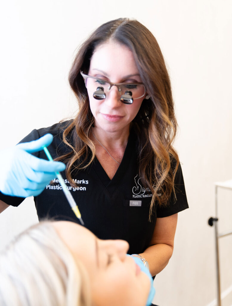 Dr. Marks injecting wrinkle relaxers or facial fillers into a female patient's forehead inside a clinic room